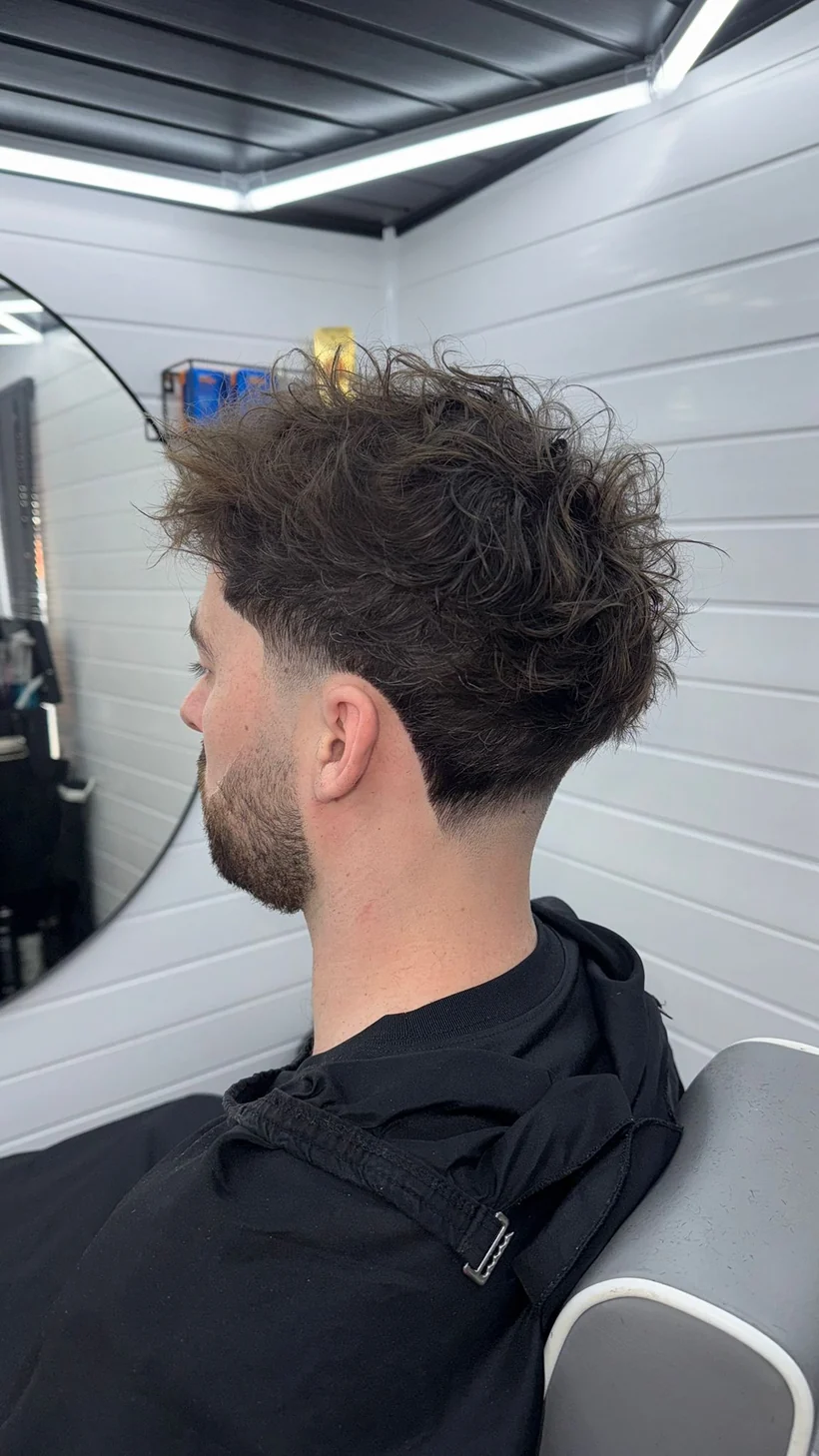 Curly length left on top over faded sides, side profile, client in a black cape